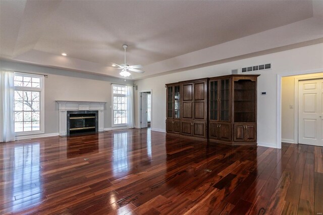 unfurnished living room with a raised ceiling, dark wood-type flooring, baseboards, ceiling fan, and a high end fireplace