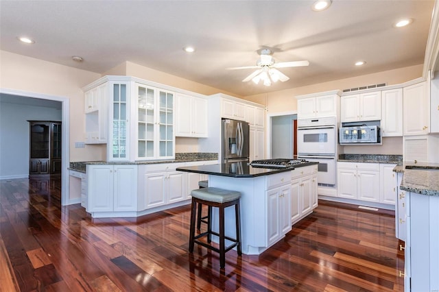 kitchen with stainless steel appliances, ceiling fan, a kitchen island, dark wood finished floors, and white cabinets