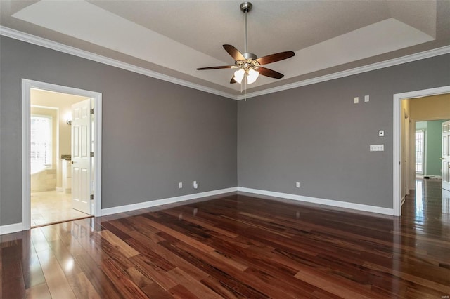 spare room with ceiling fan, wood-type flooring, a tray ceiling, crown molding, and baseboards