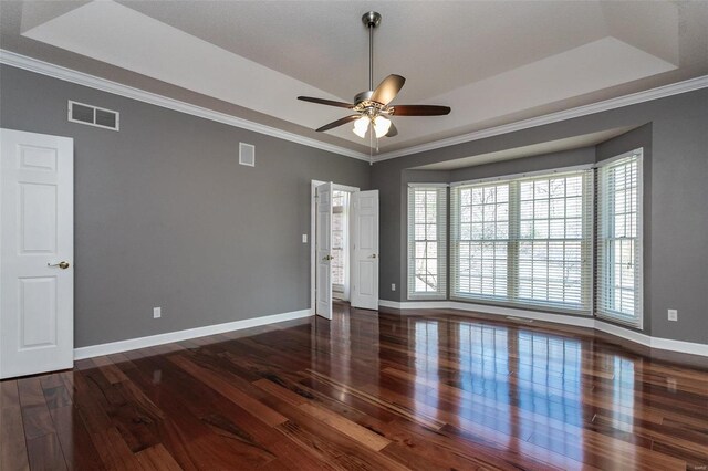 unfurnished room featuring a raised ceiling, wood finished floors, a ceiling fan, and ornamental molding