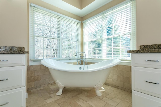 bathroom with tile walls, plenty of natural light, stone tile flooring, a freestanding tub, and a wainscoted wall
