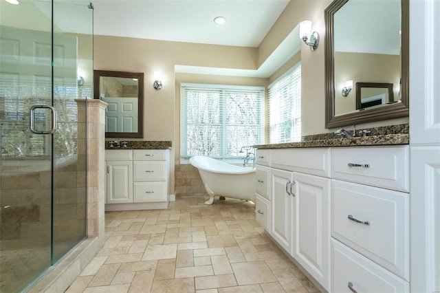 full bath with a shower stall, a soaking tub, two vanities, stone tile flooring, and recessed lighting
