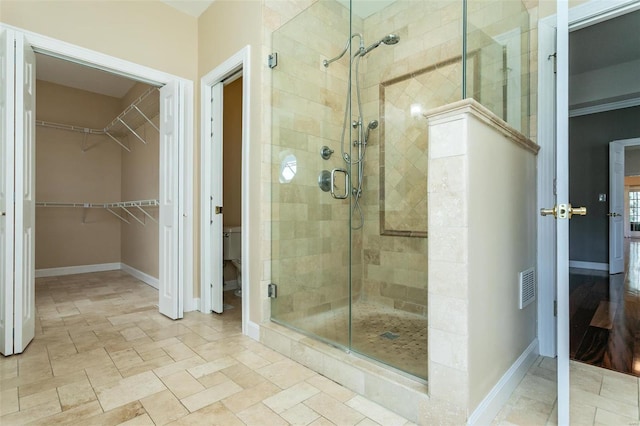 bathroom with a stall shower, a walk in closet, baseboards, and toilet