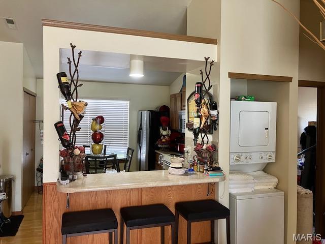 4304 Inlet Isle Dr, Florissant, MO 63034 - kitchen featuring stacked washing machine and dryer, freestanding refrigerator, light wood-style floors, a breakfast bar area, and light countertops