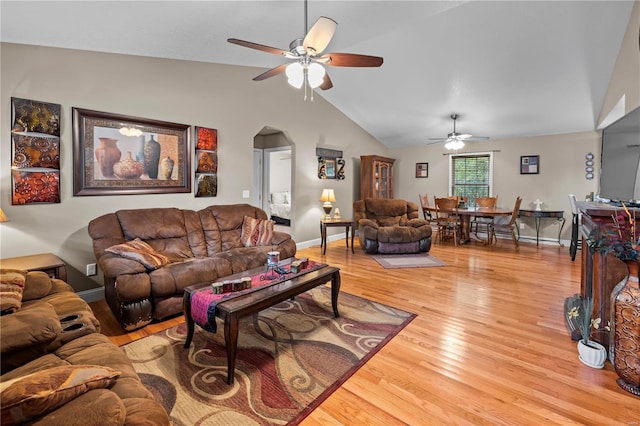 living area featuring ceiling fan, vaulted ceiling, light wood-type flooring, arched walkways, and baseboards