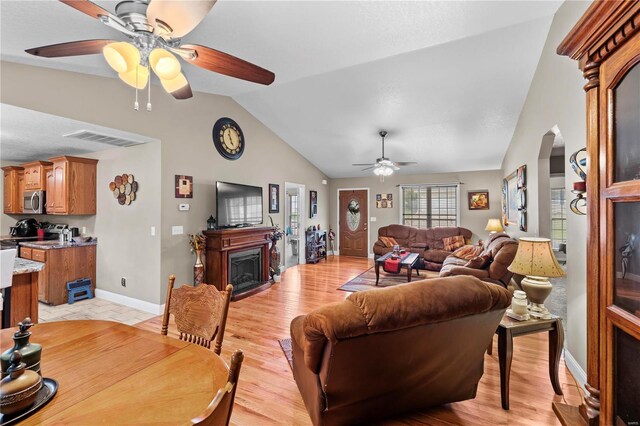 living room with a ceiling fan, lofted ceiling, arched walkways, a fireplace, and light wood-style floors