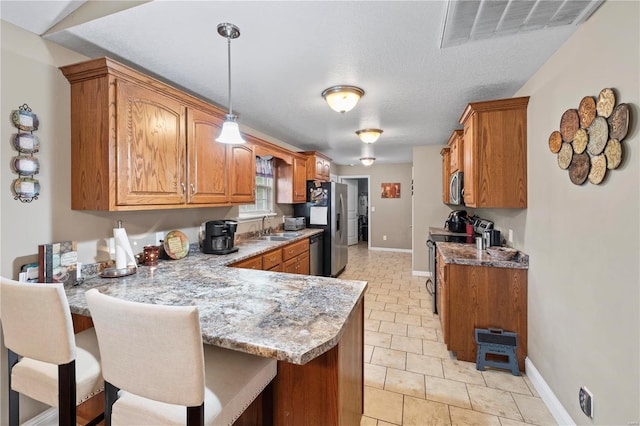 kitchen featuring appliances with stainless steel finishes, a peninsula, a sink, brown cabinets, and baseboards