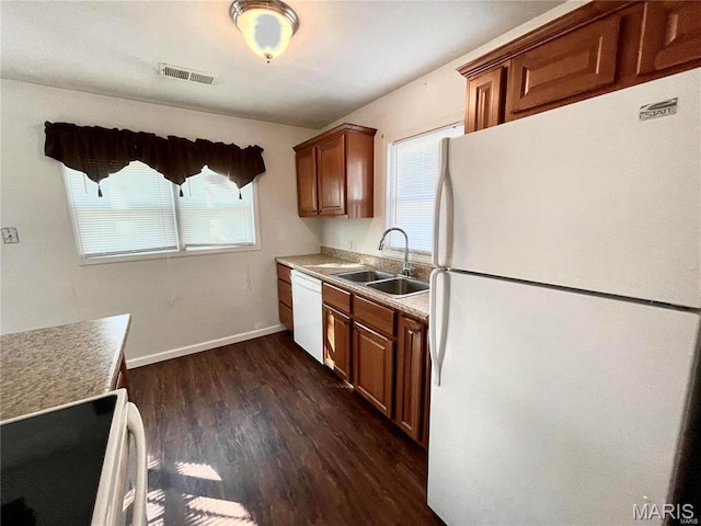 kitchen featuring white appliances, a sink, dark wood-style flooring, brown cabinets, and baseboards