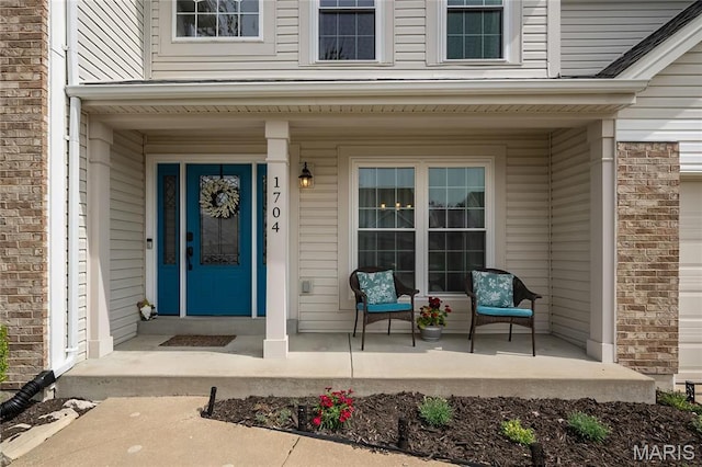 doorway to property featuring covered porch and brick siding