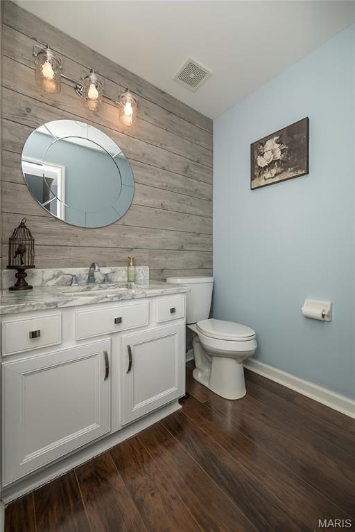 bathroom with wooden walls, baseboards, toilet, vanity, and wood finished floors