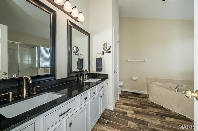 bathroom with toilet, wood finished floors, double vanity, a bath, and a shower with door