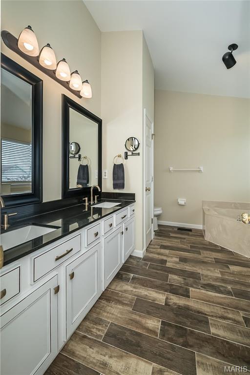 bathroom featuring wood finished floors, double vanity, toilet, a bath, and baseboards