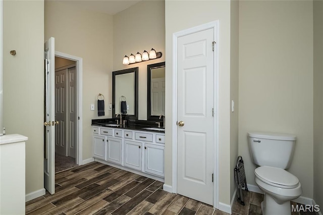 bathroom featuring wood finished floors, double vanity, baseboards, and toilet