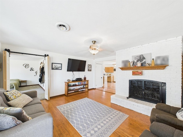 16892 Beaufort Rd, Crocker, MO 65452 - living area with a ceiling fan, wood finished floors, a barn door, a brick fireplace, and baseboards