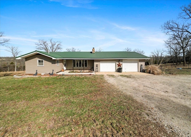 single story home featuring a chimney, dirt driveway, a front lawn, metal roof, and an attached garage