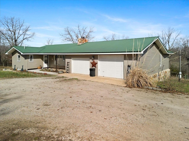 view of front facade featuring an attached garage, dirt driveway, a chimney, and metal roof
