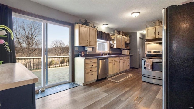 kitchen with stainless steel appliances, a sink, wood finished floors, light brown cabinets, and under cabinet range hood