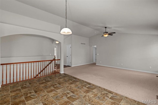 carpeted spare room with a ceiling fan, stone finish floors, baseboards, vaulted ceiling, and arched walkways