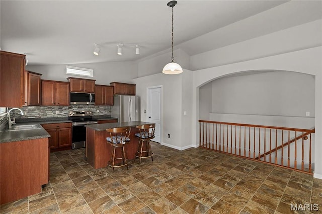kitchen with stainless steel appliances, a sink, lofted ceiling, dark countertops, and dark stone finish flooring