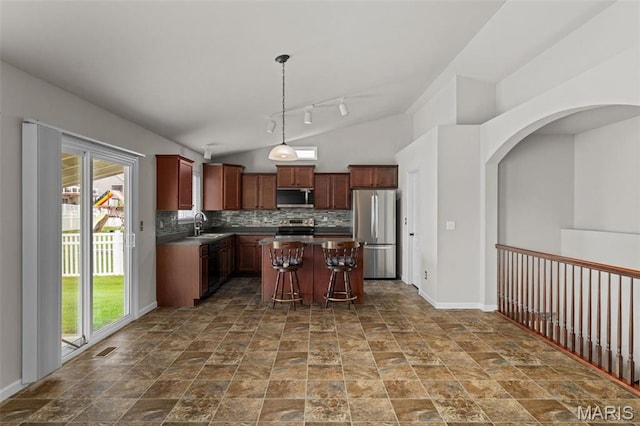 kitchen featuring stainless steel appliances, healthy amount of natural light, a kitchen island, vaulted ceiling, and backsplash