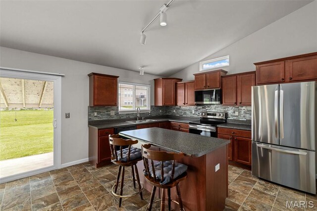 kitchen featuring appliances with stainless steel finishes, dark countertops, backsplash, a sink, and a kitchen bar