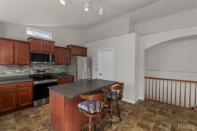 kitchen featuring appliances with stainless steel finishes, dark countertops, a center island, tasteful backsplash, and a kitchen breakfast bar
