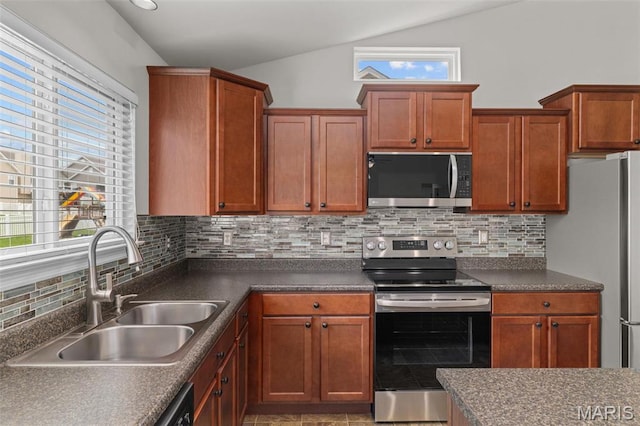 kitchen featuring stainless steel appliances, a sink, vaulted ceiling, backsplash, and dark countertops