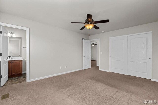 unfurnished bedroom featuring carpet flooring, baseboards, a closet, ensuite bath, and a ceiling fan