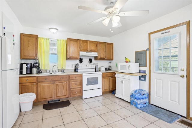 kitchen with white appliances, a sink, under cabinet range hood, light countertops, and brown cabinets