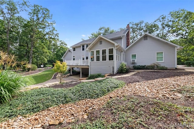 rear view of house featuring a chimney, a wooden deck, and a sunroom