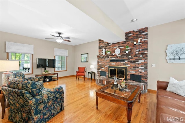 living room with wood finished floors, a brick fireplace, a ceiling fan, and baseboards