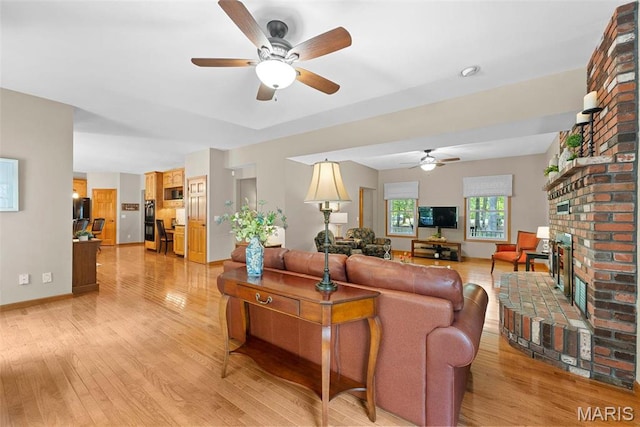 living room featuring ceiling fan, light wood-style flooring, a brick fireplace, and baseboards