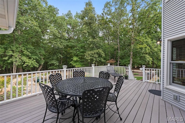 wooden terrace featuring outdoor dining area and view of wooded area