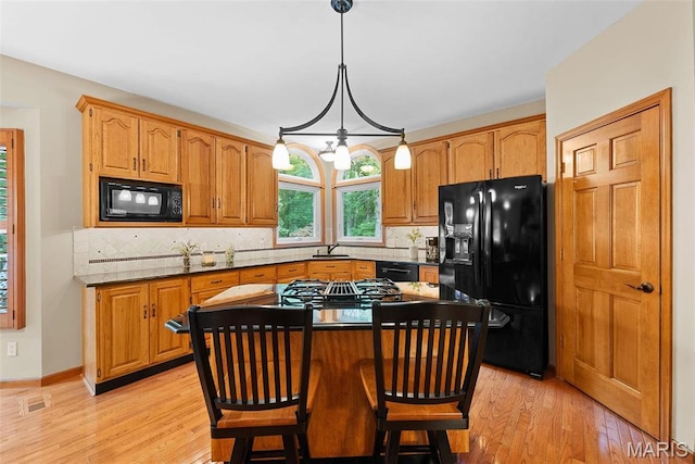 kitchen with black appliances, light wood-style floors, a kitchen island, and tasteful backsplash