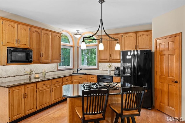 kitchen with black appliances, decorative backsplash, light wood-style floors, a breakfast bar area, and pendant lighting