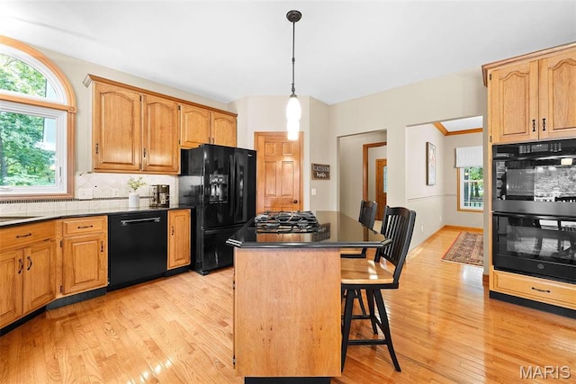 kitchen with black appliances, dark countertops, light wood finished floors, a kitchen bar, and a center island