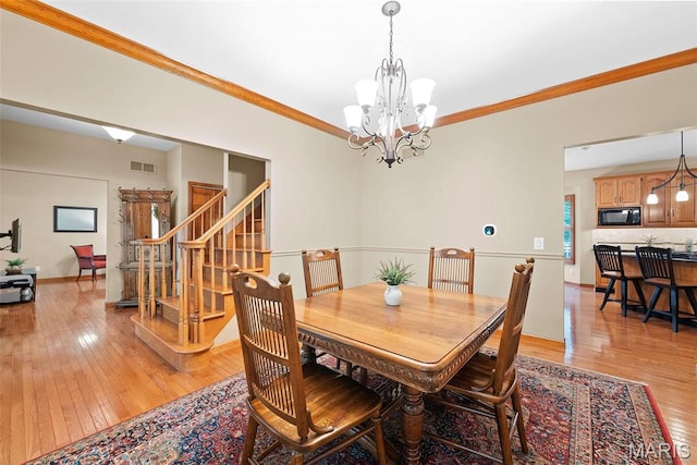 dining area with light wood-style flooring, a chandelier, stairs, and ornamental molding