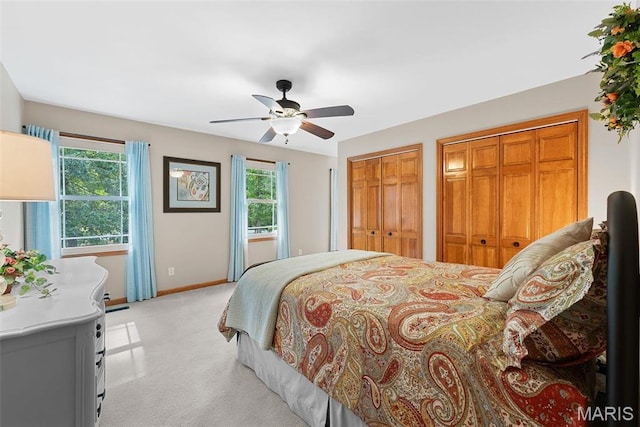 bedroom featuring light colored carpet, two closets, baseboards, and a ceiling fan