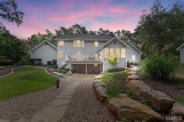 back of house at dusk featuring stairs, a lawn, and a deck