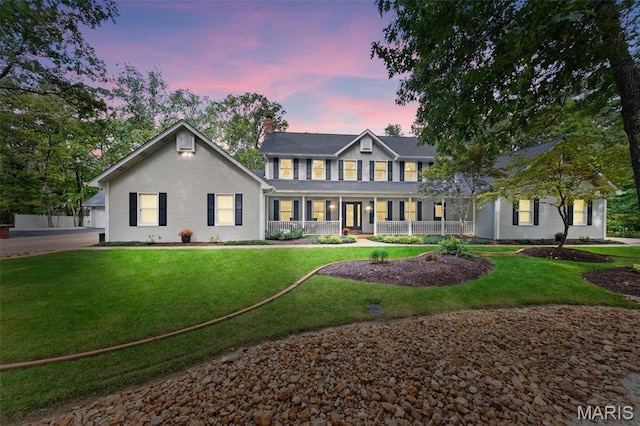 colonial-style house featuring covered porch, a chimney, and a yard