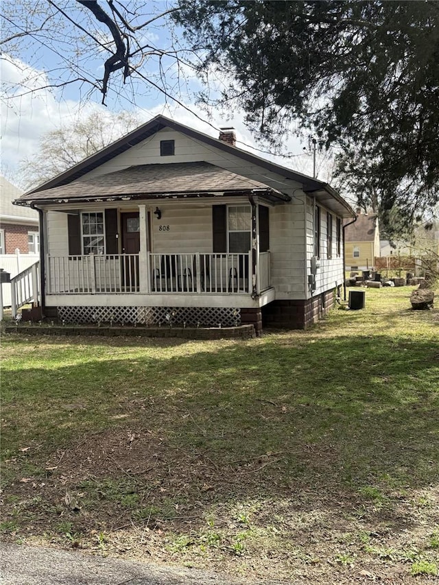 view of front of home featuring a porch, a front lawn, and a chimney