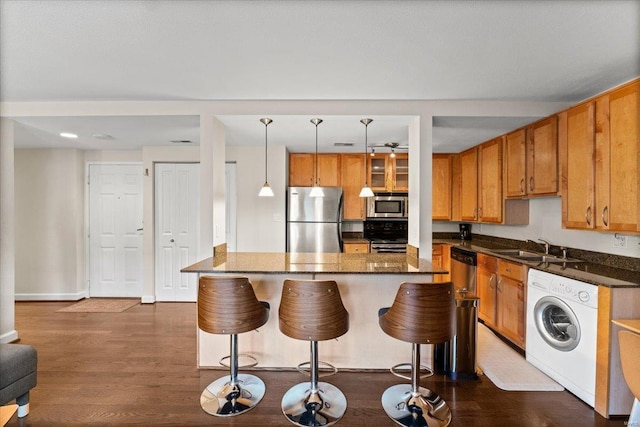 kitchen featuring appliances with stainless steel finishes, washer / clothes dryer, a sink, dark wood-type flooring, and a kitchen breakfast bar