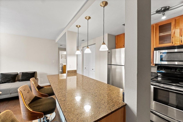 kitchen with stainless steel appliances, brown cabinets, open floor plan, and stone countertops