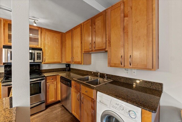 kitchen featuring washer / clothes dryer, appliances with stainless steel finishes, a sink, wood finished floors, and glass insert cabinets