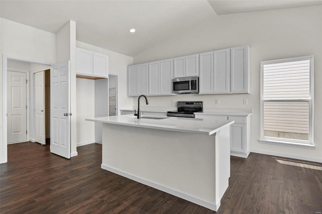 kitchen featuring appliances with stainless steel finishes, a sink, vaulted ceiling, light countertops, and a center island with sink