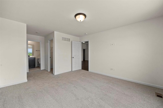 unfurnished bedroom with light colored carpet, baseboards, and ensuite bathroom