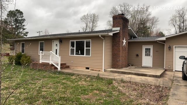 back of property featuring a chimney, a lawn, an attached garage, and crawl space