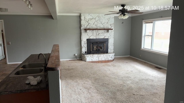unfurnished living room with a sink, ceiling fan, crown molding, carpet flooring, and baseboards