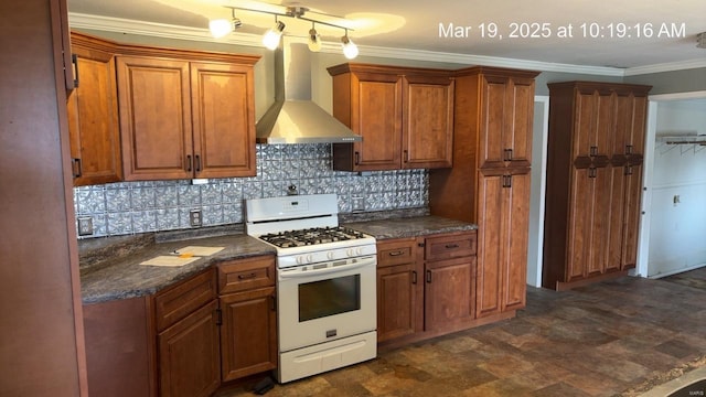 kitchen with white gas range oven, wall chimney range hood, backsplash, brown cabinets, and ornamental molding