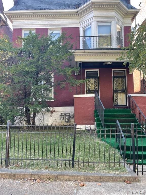 second empire-style home with a balcony, a fenced front yard, brick siding, covered porch, and a high end roof